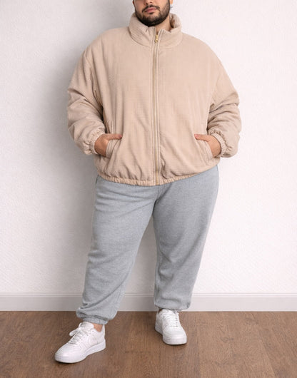 Person wearing a beige Plus Size Mens Puffer Jacket and gray pants standing against a white wall.