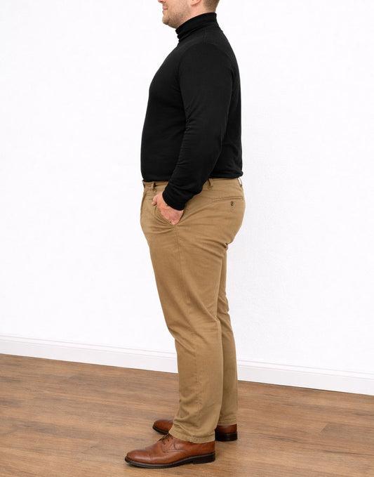 Side view of man wearing a black Plus Size Mens Turtleneck Long Sleeve Top and tan pants standing on a wooden floor with a white wall background.