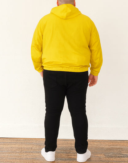 Back view of person wearing a yellow Plus Size Mens Windbreaker Jacket and black pants standing against a white wall.