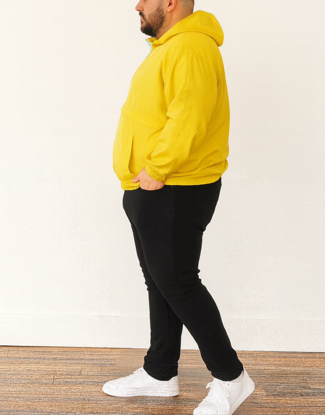 Side view of person wearing a yellow Plus Size Mens Windbreaker Jacket and black pants standing against a white wall.