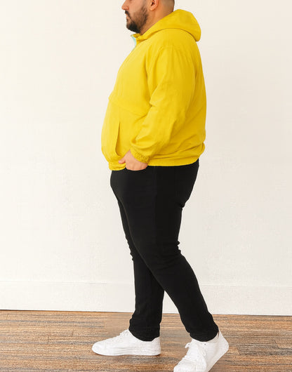 Side view of person wearing a yellow Plus Size Mens Windbreaker Jacket and black pants standing against a white wall.