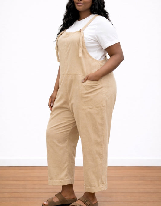 Side view of woman wearing beige Plus Size Overall Jumpsuit and a white shirt on a white background.