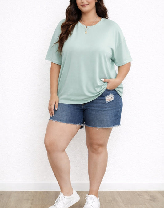 Woman wearing a light green Plus Size Oversized Crew Neck T-Shirt and denim shorts on a white background