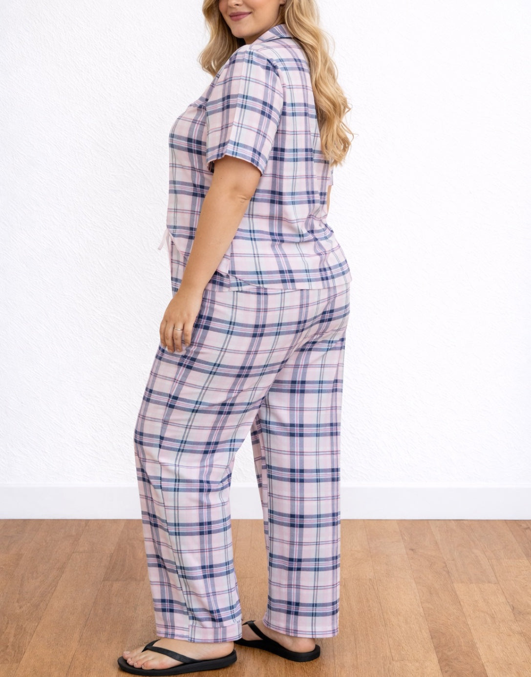 Side view of woman wearing a plaid pajama top and Plus Size Pajama Pants on a wooden floor with a white background