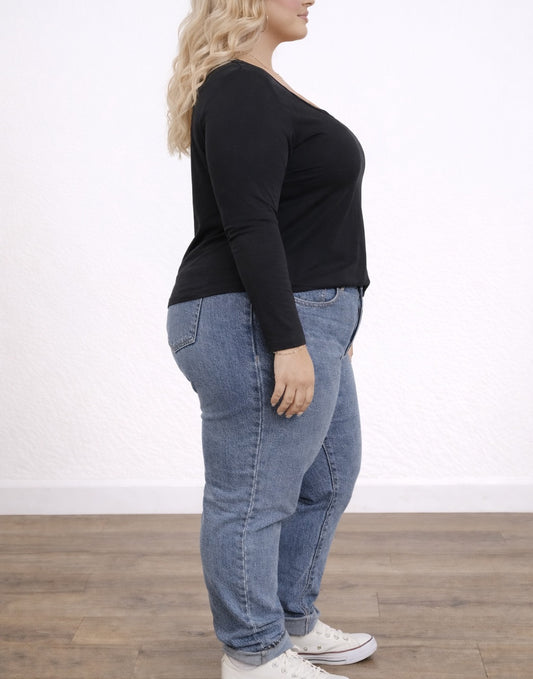 Side view of woman wearing a black Plus Size Scoop Neck Long Sleeve Top and blue jeans on a plain background.