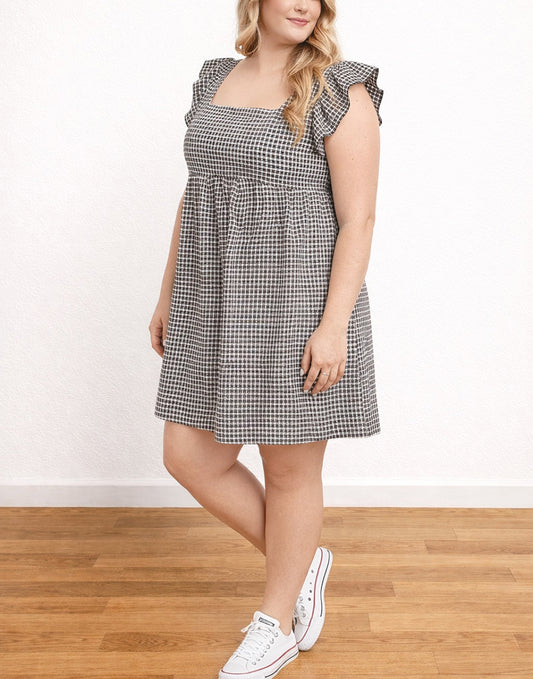 Side view of woman wearing a black and white checkered Plus Size Square Neck Smock Dress with ruffled sleeves on a wooden floor.