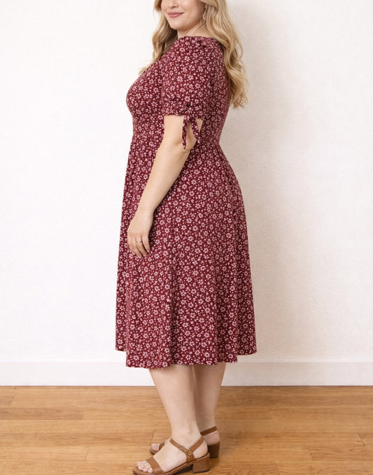 Side view of woman wearing a red floral Plus Size Tie Sleeve Button Front Midi Dress standing against a white wall.
