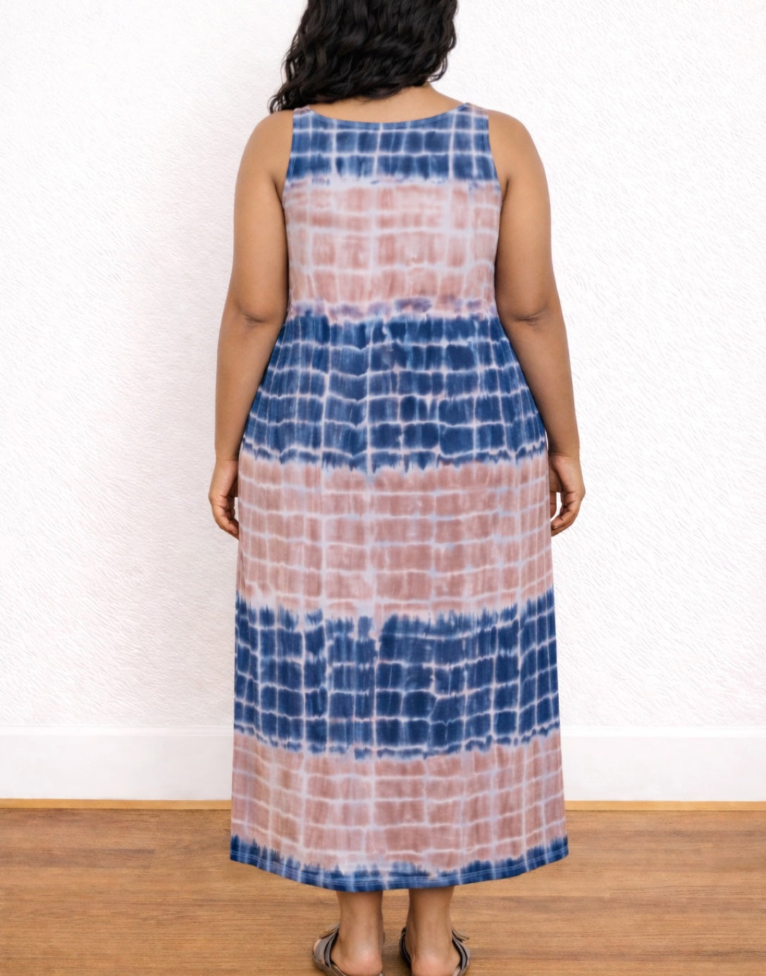 Back view of woman wearing a tie-dye Plus Size Tank Dress with blue and pink patterns against a white wall.