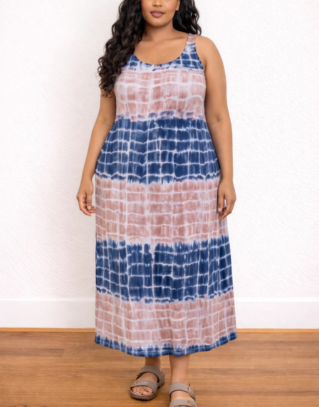 Woman wearing a tie-dye Plus Size Tank Dress with blue and pink patterns against a white wall.