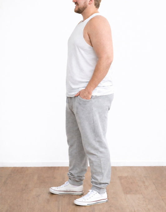 Side view of man wearing a white Plus Size Workout Tank Top and gray sweatpants standing against a white wall.