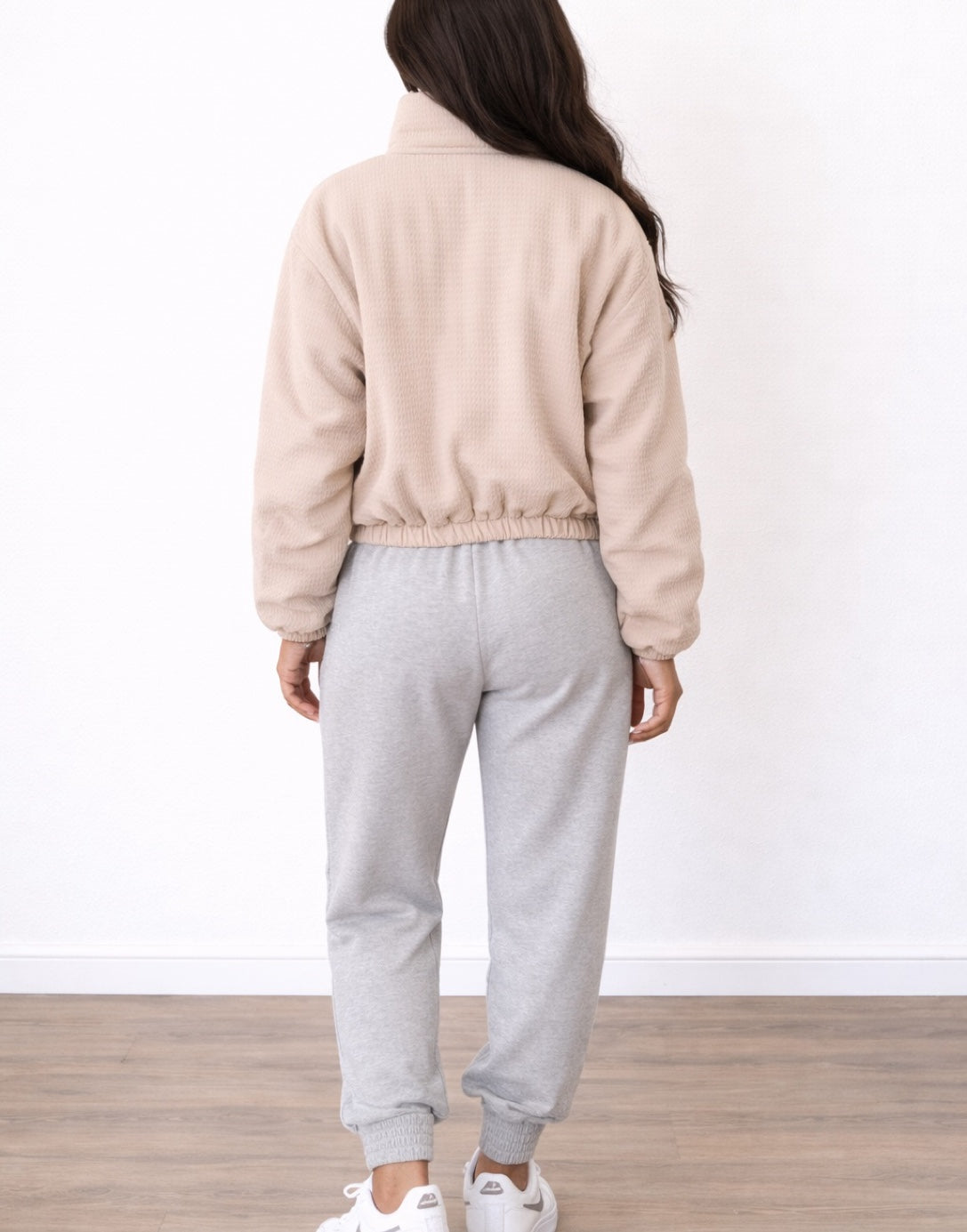 Back view of woman wearing a beige Puffer Jacket and gray sweatpants on a white background.