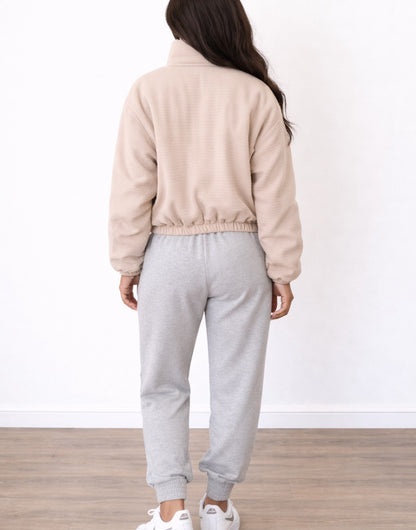 Back view of woman wearing a beige Puffer Jacket and gray sweatpants on a white background.