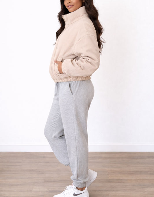 Side view of woman wearing a beige Puffer Jacket and gray sweatpants on a white background.