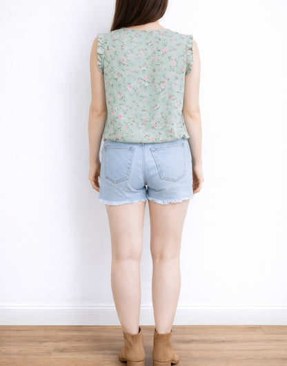 Back view of woman wearing a floral Ruffled Sleeveless Blouse and denim shorts against a white background.