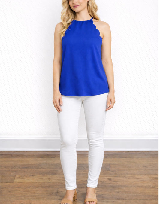 Woman wearing a blue Scallop Halter Top and white pants on a plain background.
