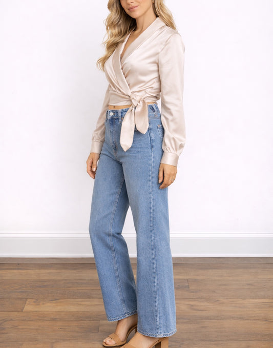 Side view of woman wearing a beige Shawl Collar Wrap Blouse and blue jeans against a white background.
