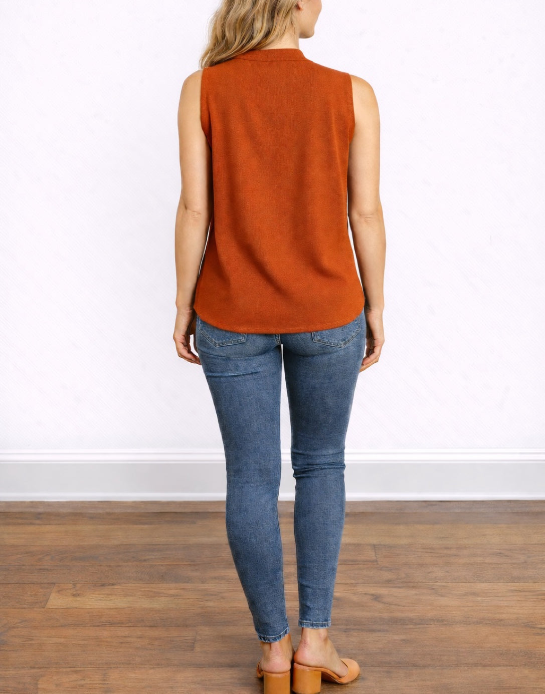 Back view of woman wearing a rust-colored Sleeveless Blouse and blue jeans on a white background.