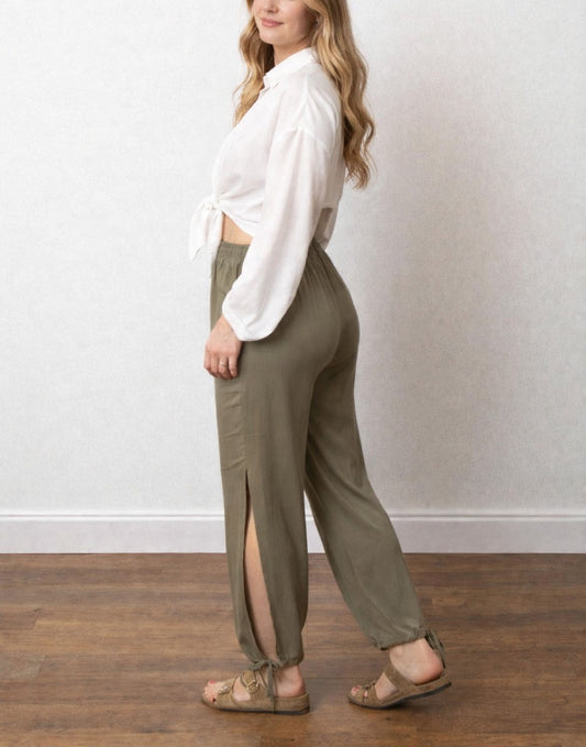 Side view of woman wearing green Side Tie Pants with an elasticized waistband, standing in a white room with a wooden floor.