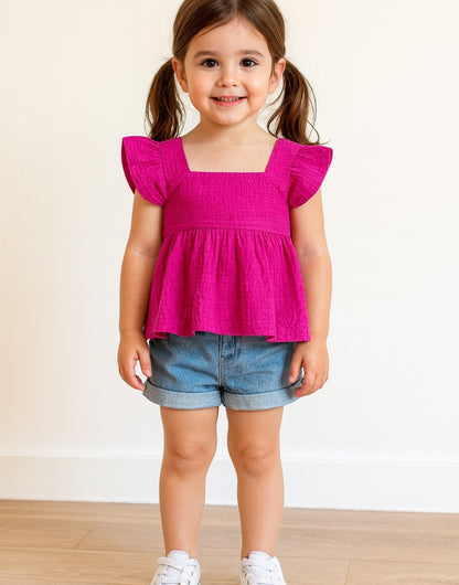 Young girl wearing a bright pink Square Neck Short Sleeve Peplum Top and denim shorts on a plain background
