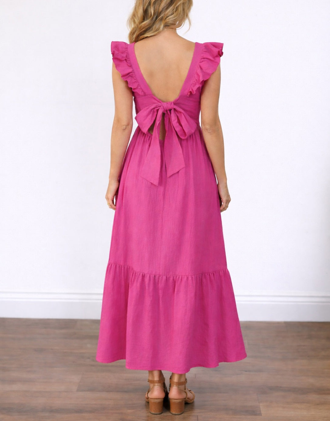 Back view of woman wearing a pink Ruffled Sleeve Maxi dress with cut-out back and tied waist on a beige background.