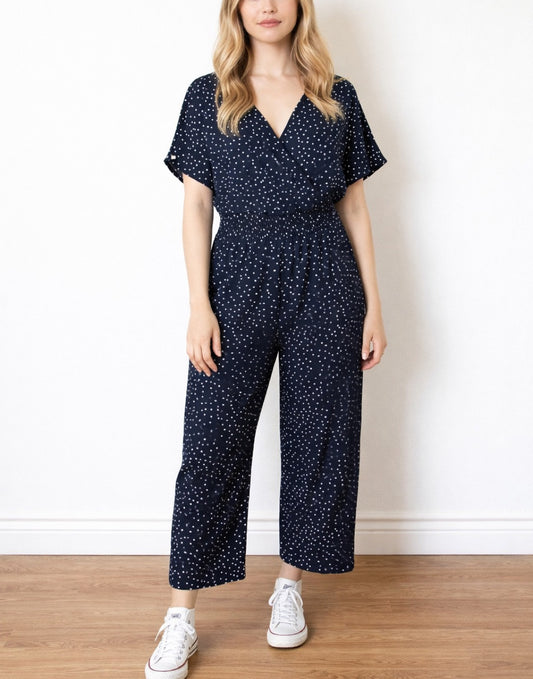 Woman wearing a navy blue Surplice Jumpsuit with white polka dots on a plain background.
