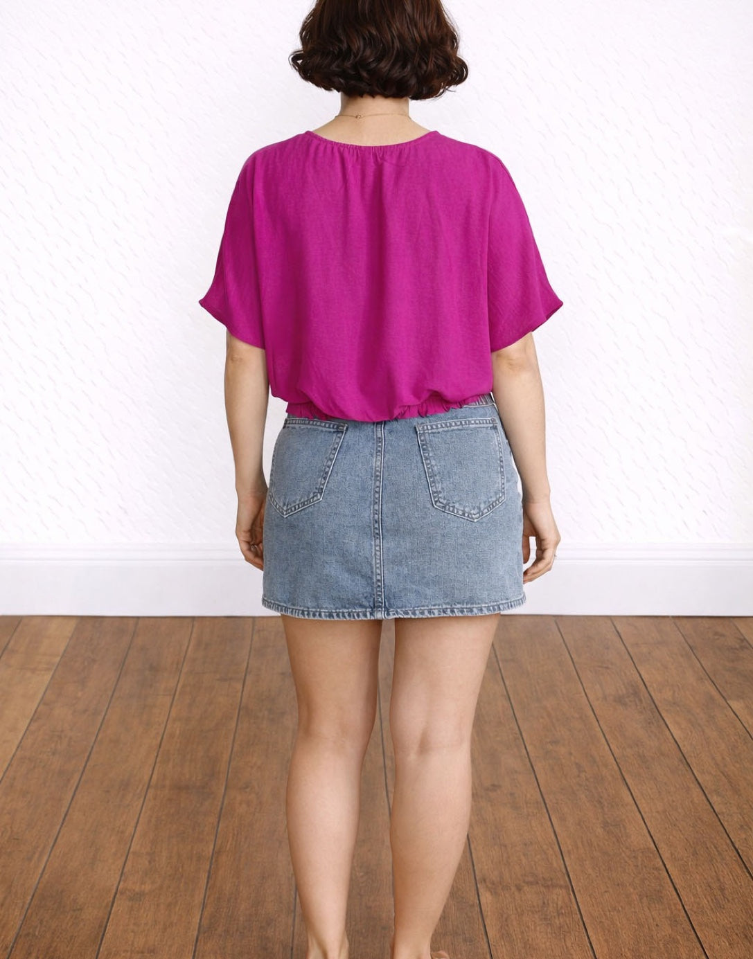 Back view of woman wearing a bright pink Surplice Kimono Sleeve Crop Blouse and denim skirt on a white background.