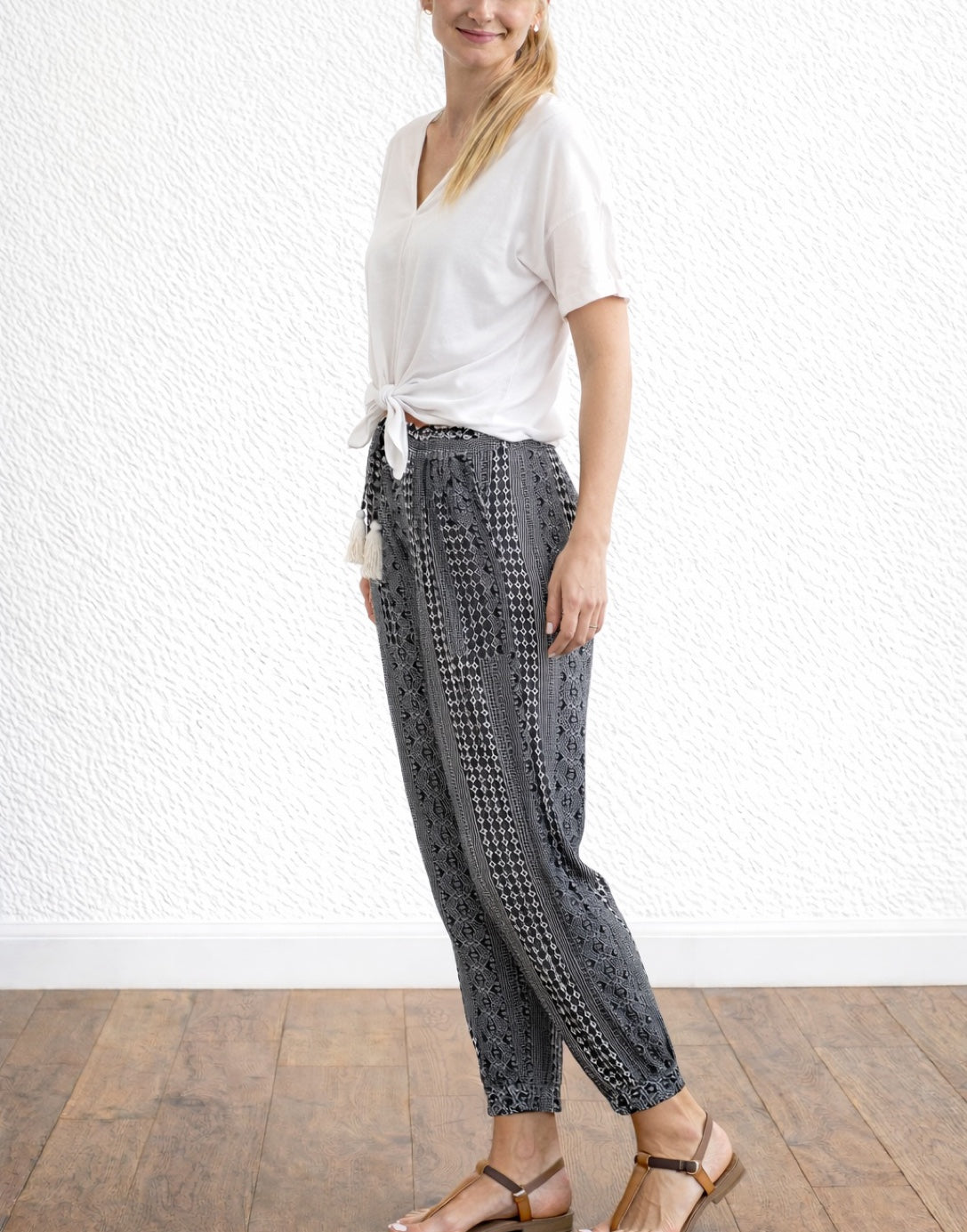 Side view of woman wearing a tie front tee with black and white patterned Tassel Tie Paperbag Pants against a plain background.