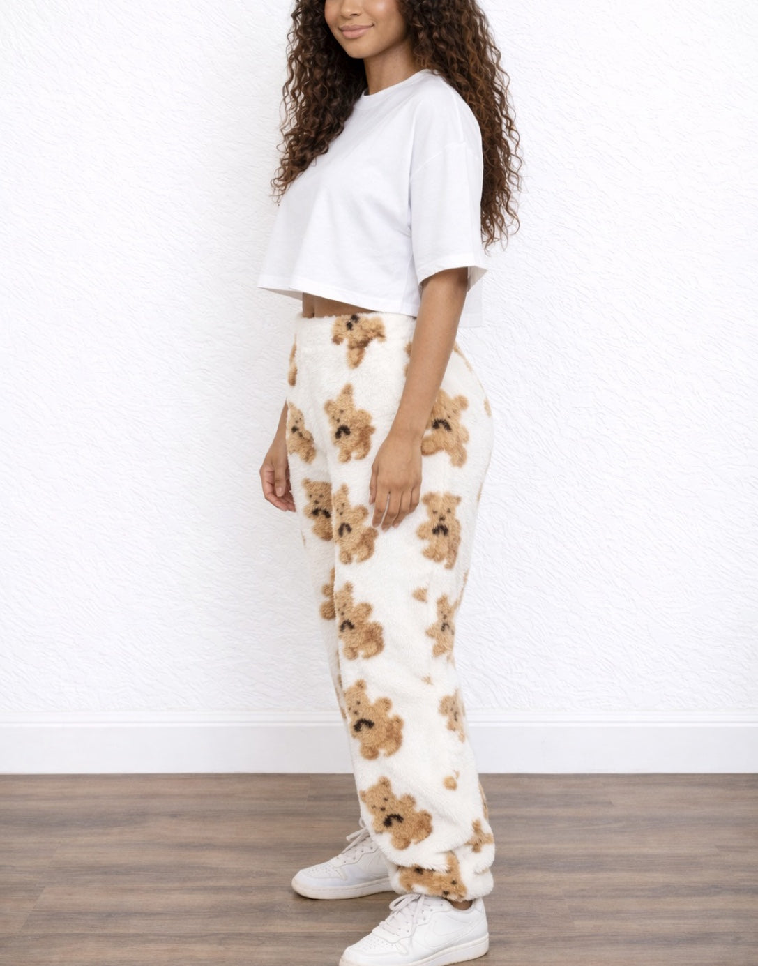 Side view of woman wearing a white top and white Teddy Pants with teddy bear pattern on a wooden floor.
