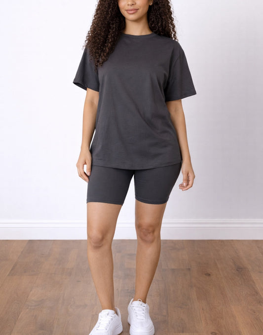 Woman wearing a dark gray Tee and Biker Shorts Set with white sneakers on a wooden floor.