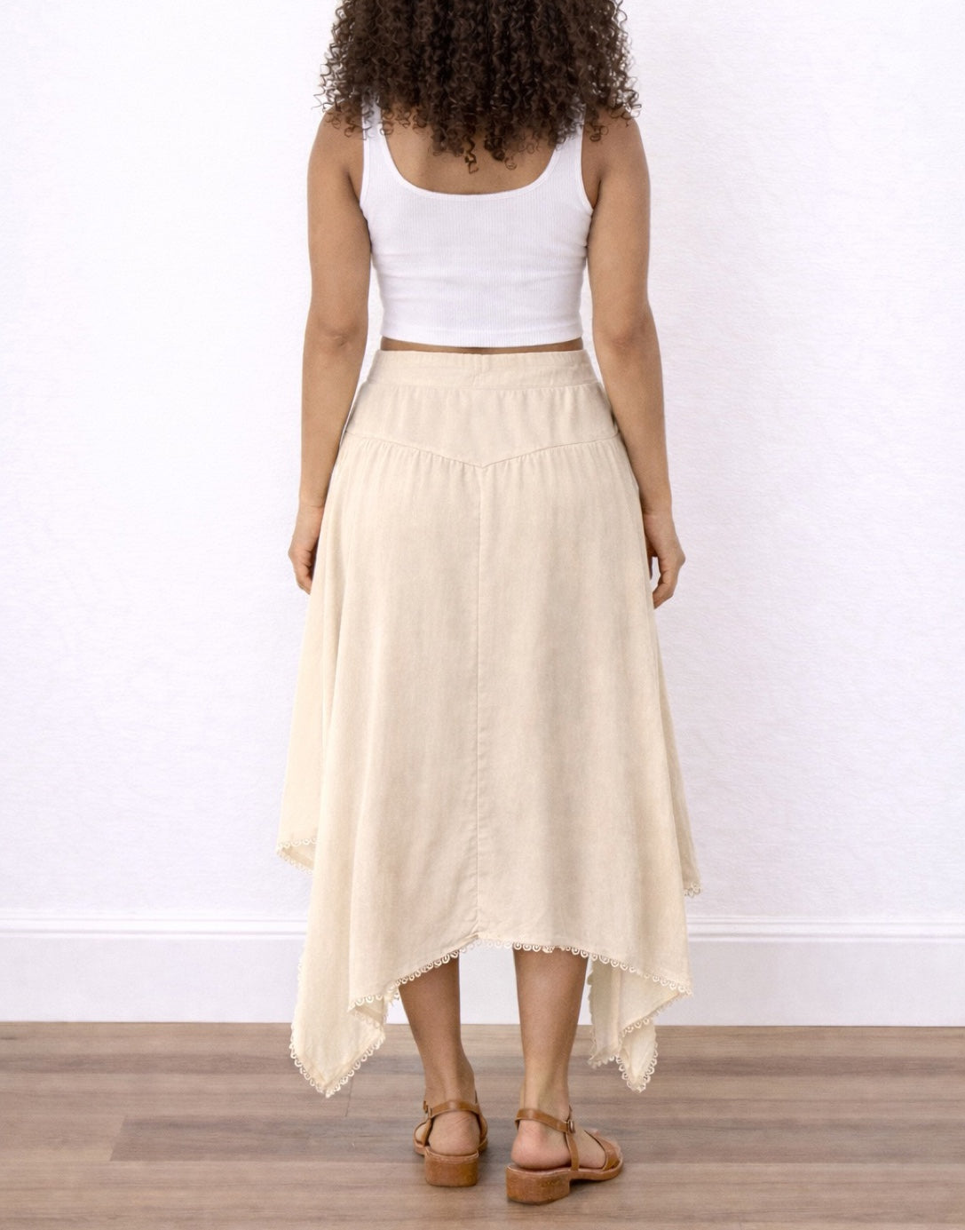 Back view of woman wearing a white top and beige Tie Front Asymmetrical Hem Skirt on a plain background.