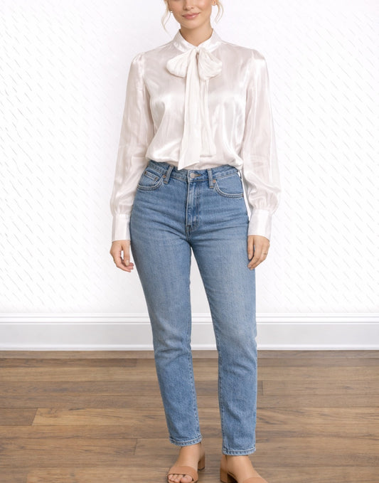Woman wearing a white Tie Neck Puff Long Sleeve Blouse with a bow and blue jeans on a plain background.