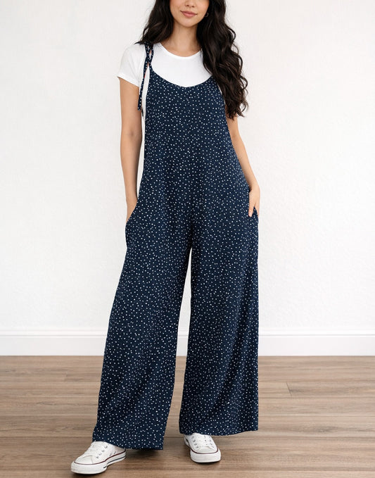 Woman wearing navy Tie Shoulder Jumpsuit with white polka dots and white tee underneath on plain white background.