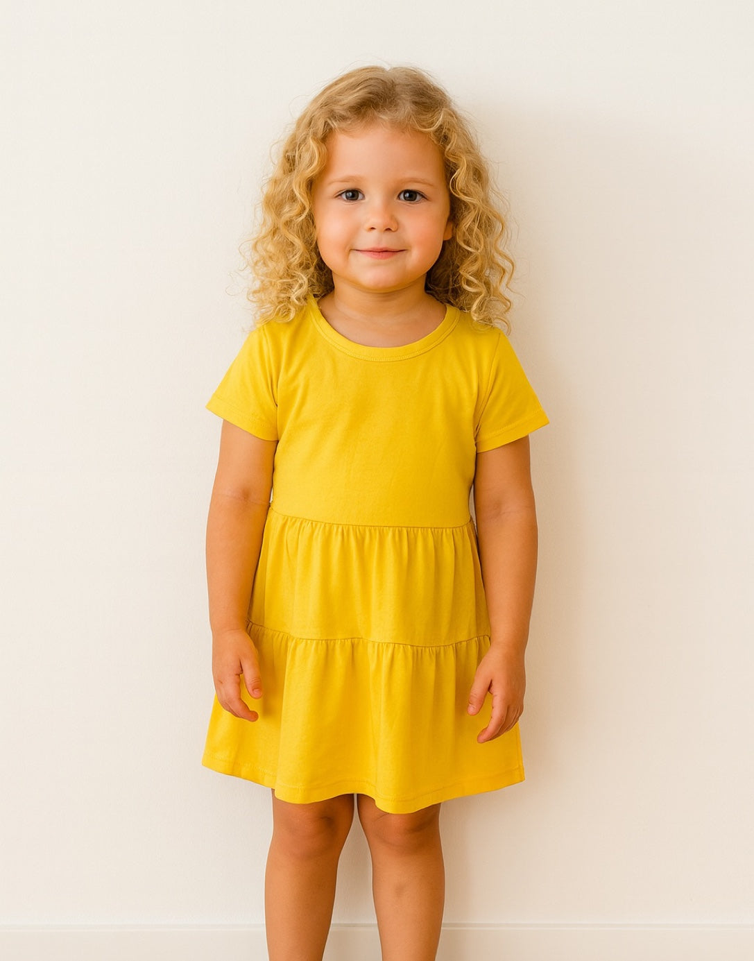 Young girl wearing a yellow Ruffle Hem T-Shirt Dress against a white background