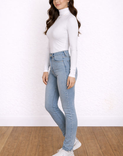 Side view of woman wearing light blue jeans and a white Turtleneck Long Sleeve Top against a white background.