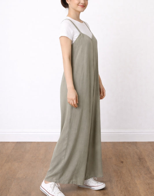 Side view of woman wearing a green Wide Leg Suspender Jumpsuit and white shirt on a plain background.