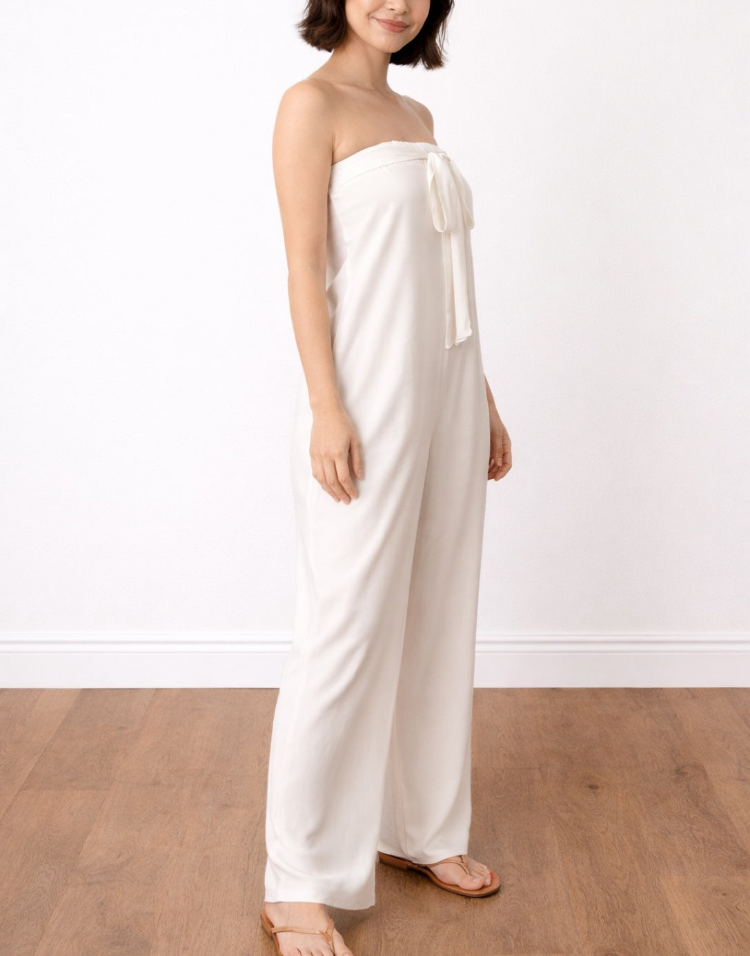 Side view of woman wearing a white strapless Wide Leg Tube Jumpsuit on a plain background.