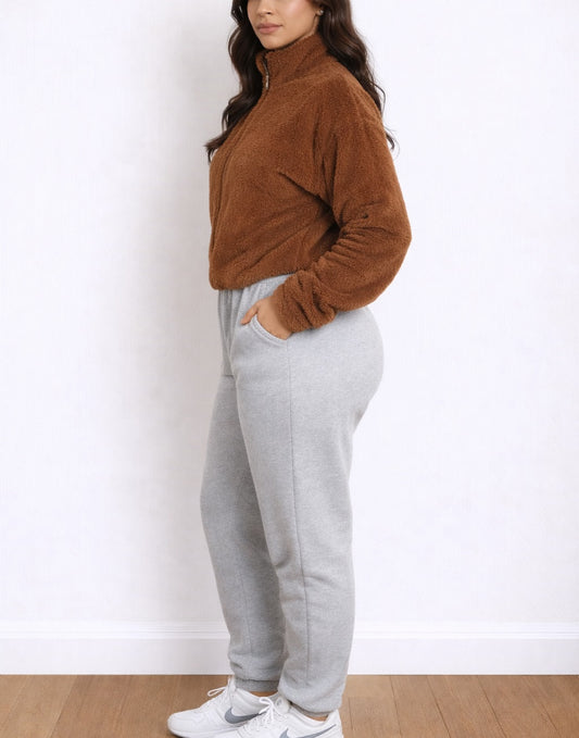Side view of woman wearing a brown zip-up Bomber Crop Jacket and gray sweatpants on a white background.